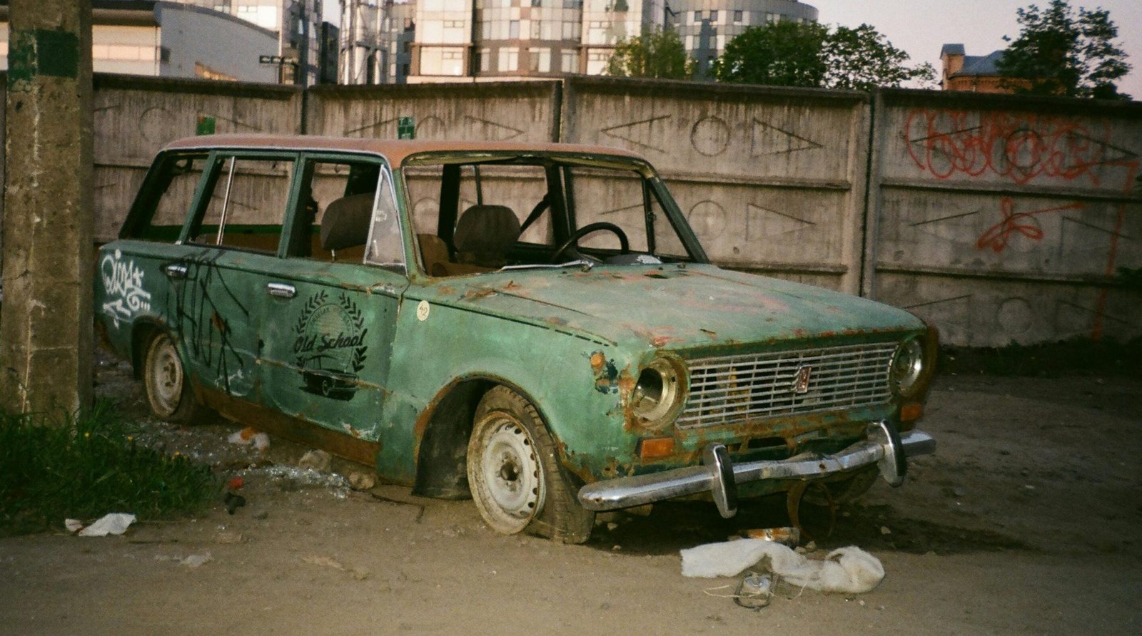 Abandoned vintage car in urban area with graffiti and rust.