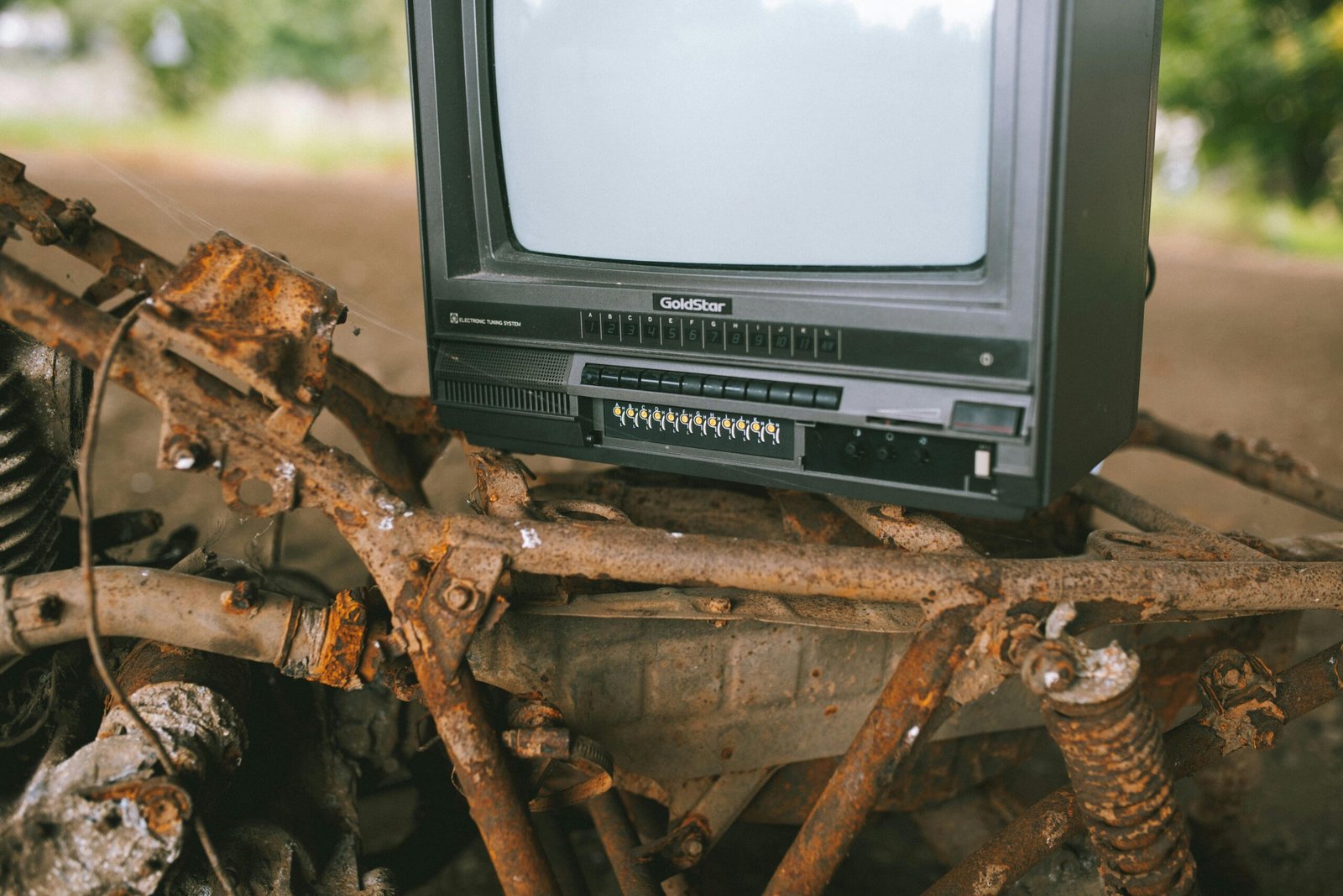 A retro television placed on a corroded bicycle frame, evoking nostalgia and decay outdoors.