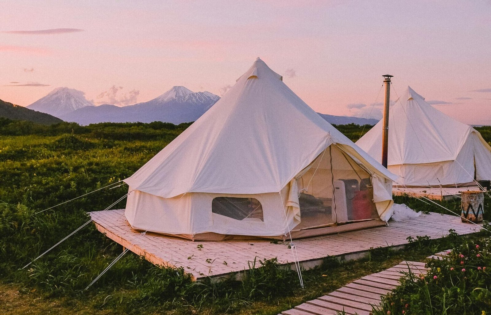 Explore the serene landscape of Kamchatka with white tents and stunning mountains at sunset.
